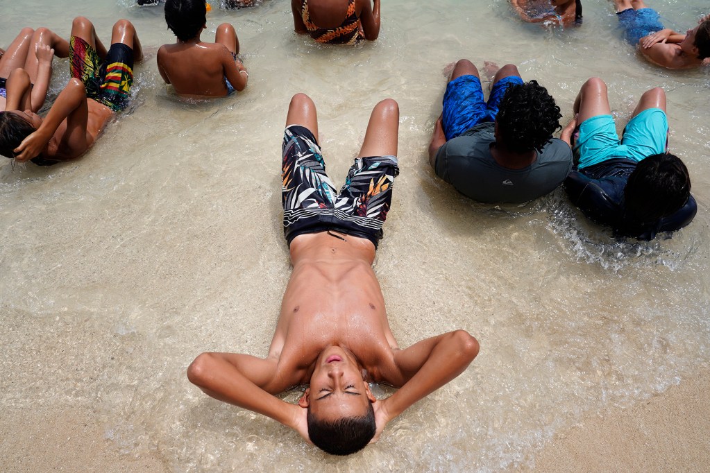 Bentley Collman, 15, does crunches on the shore during Honolulu Ocean Safety Department’s Junior Lifeguard Program beach-fitness exercise Kainoa McGee calls, “The Burn,” during its weeklong program at Ko’olina Wednesday, June 25, 2025, in Kapolei. (Kevin Fujii/Civil Beat/2025)