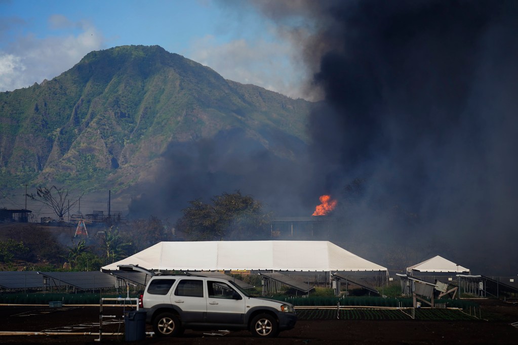 A Māʻili vegetation fire reaches a structure Sunday, July 6, 2025, in Waiʻanae. A mandatory evacuation order was issued mauka of Kulaaupuni Road. According to the Honolulu Fire Department, the fire is reported to be 75% contained at 7:25 p.m.. Almost 100 acres have burned, with some structures damaged and a woman transported to the hospital with burns and smoke inhalation. (Kevin Fujii/Civil Beat/2025)