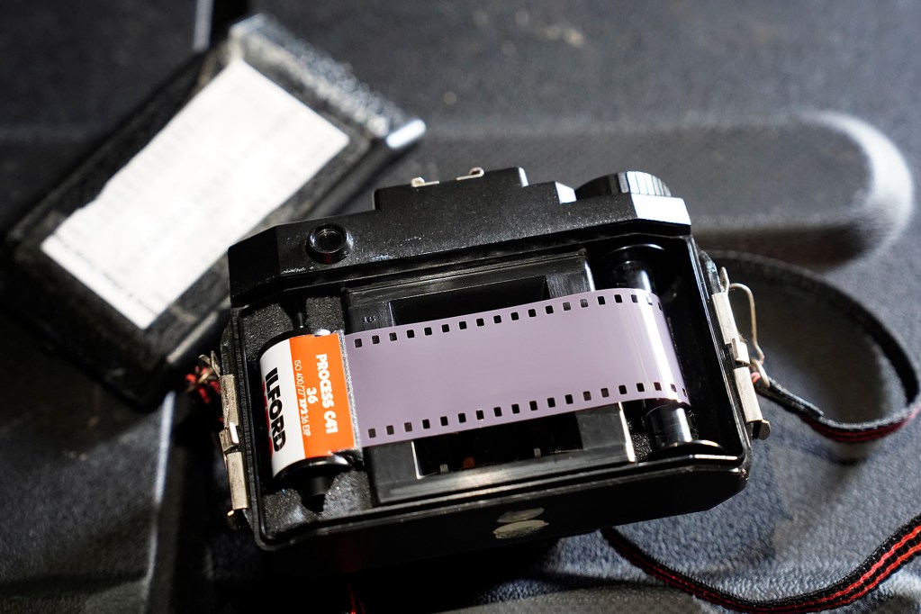 Before putting on the back of the camera, the leader of a roll of 35mm film is wrapped around a take-up spool in a  Holga 120 toy film camera and checked to ensure it’s winding Tuesday, June 15, 2025, in ʻEwa Beach. The internal frame-size mask has been removed to give the horizontal 35mm film more exposure area. The space above and below the film show an approximate depth of 120 film which are lost because of 35mm film’s horizontal dimension. But this shows how the film around the perforations or sprockets are exposed. These photos are made for John Hill’s project on child abuse. The photos are of places where alleged abuse took place. (Kevin Fujii/Civil Beat/2025)