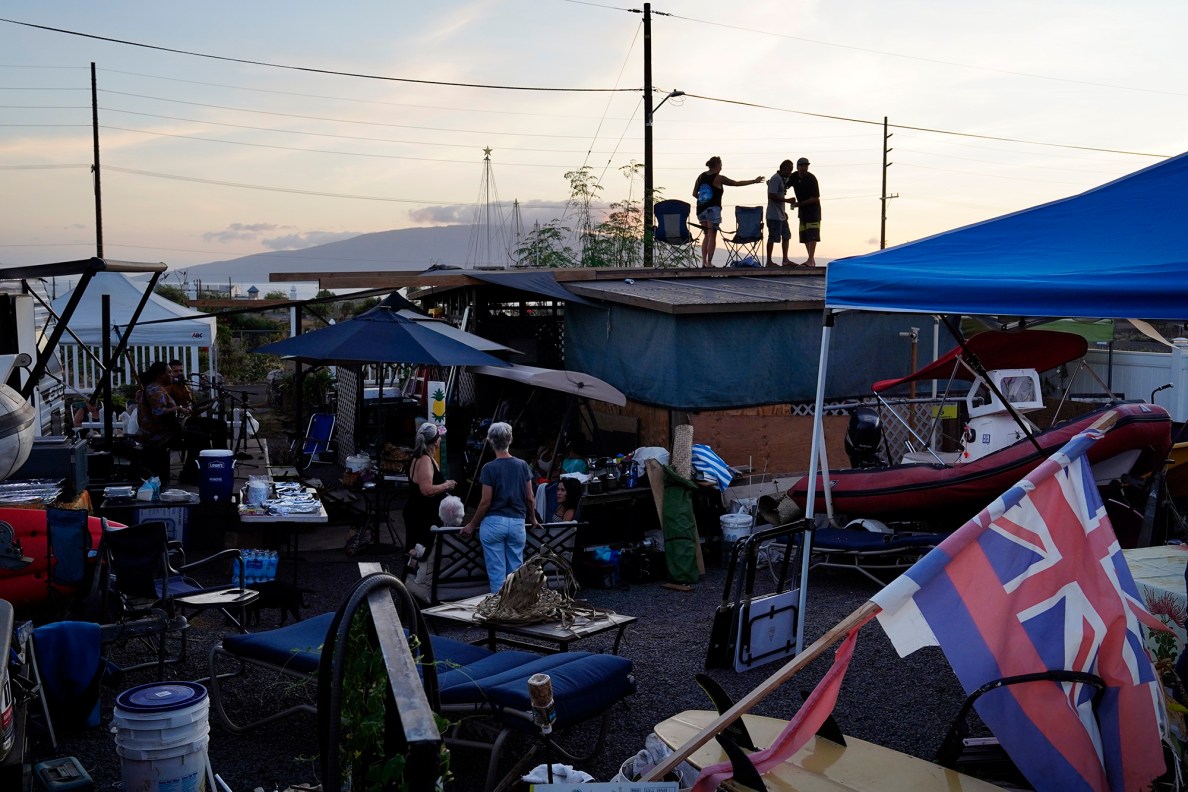 Mario Siatris, center, shows Bob and Sarah Jones the lofty view from the top of the gazebos during Mario’s 60th birthday Saturday, Aug. 2, 2025, in Lahaina. The three built the structures on Siatris’ lot after the Aug. 8, 2023, fire destroyed his home, neighborhood and town. A handful of structures stand in various stages of production. Utilities such as power lines have also been installed above ground. (Kevin Fujii/Civil Beat/2025)