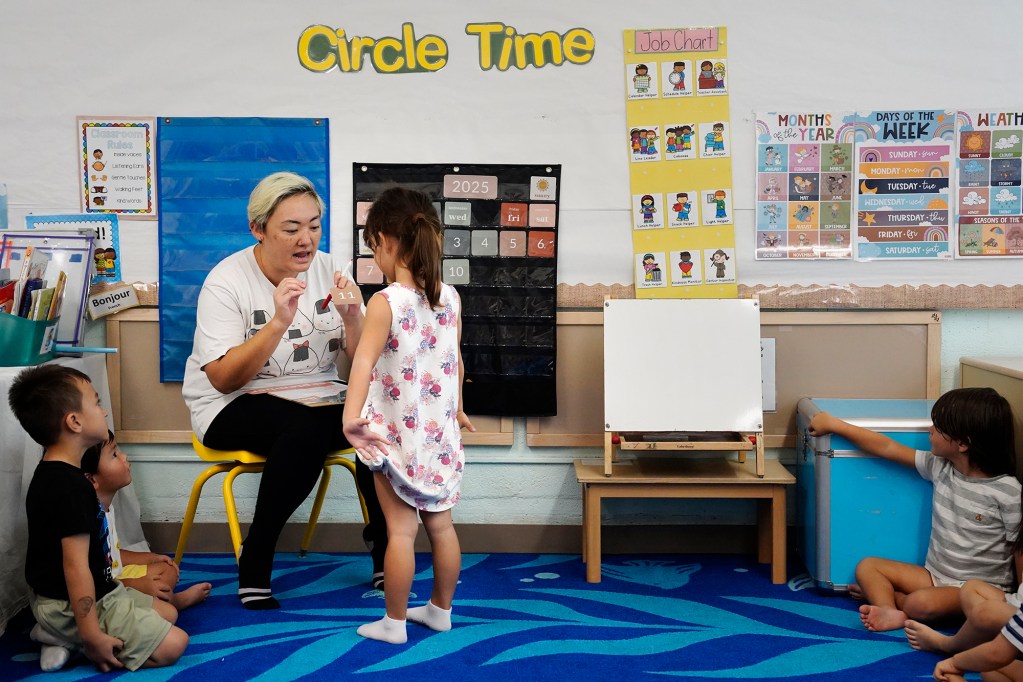 Waikīkī Community Center Preschool teacher Ryna Ota gets help with the calendar from Aria Olsson Thursday, Sept. 11, 2025, in Honolulu. (Kevin Fujii/Civil Beat/2025)