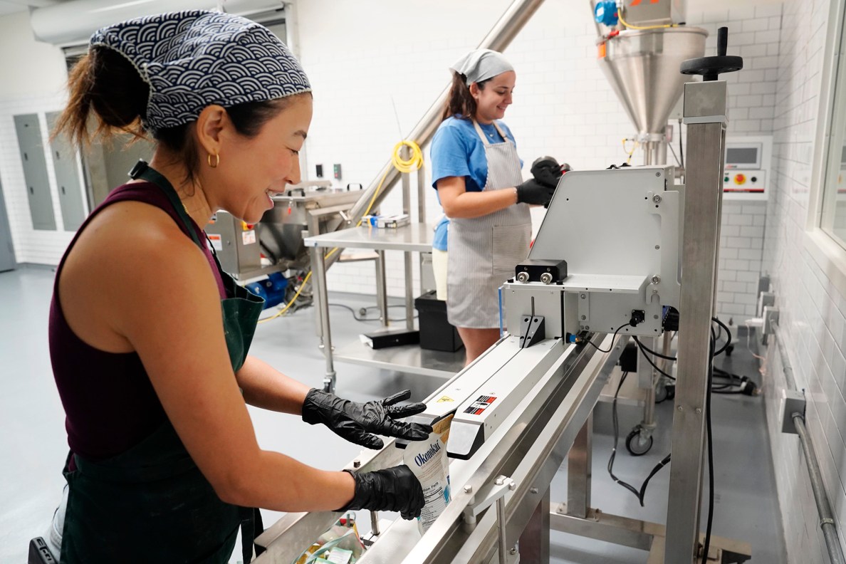Jina Wye, founder and CEO of Okonokai and her assistant Grace Gregg seal her limu cracker bags at the Wahiawā Value-Added Product Development Center Wednesday, Sept. 17, 2025, in Wahiawā. The center makes producing her “Made in Hawaiʻi” crackers easier with facilities and amenities usually owned by mass-production companies. (Kevin Fujii/Civil Beat/2025)