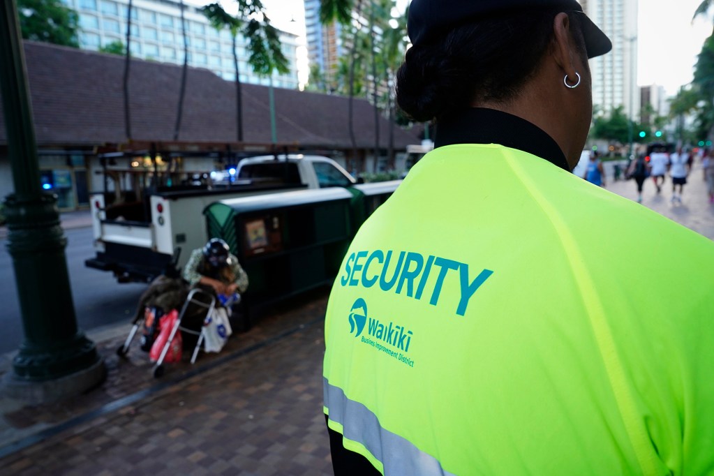 Waikīkī Business Improvement District Elevated Security guard Thoren Nansen waits for Tina, a homeless woman, to move off the sidewalk Thursday, Sept. 25, 2025, in Honolulu. They remind homeless it is illegal to loiter on the public street and sidewalk. (Kevin Fujii/Civil Beat/2025)