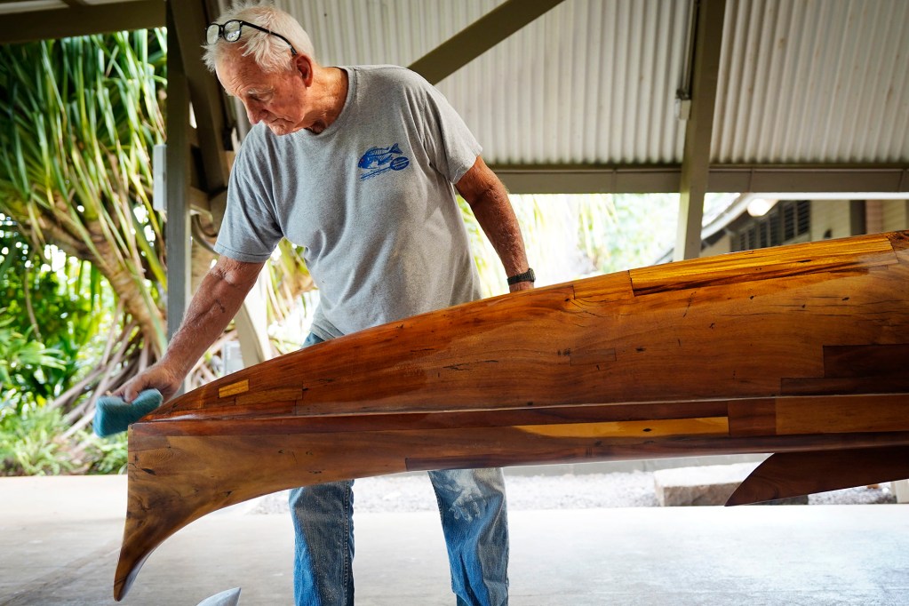 Tay Perry smoothes out the final coat on Prince Jonah Kūhiō Kalanianaʻole’s a‘a Monday, Nov. 3, 2025, at the Bishop Museum in Honolulu. The 40-foot racing canoe will return to the water for the first time in more than a decade. (Kevin Fujii/Civil Beat/2025)