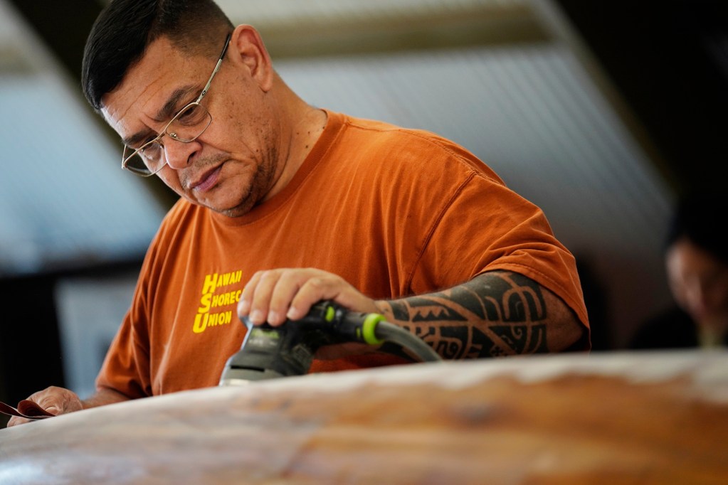 Ryan Olivares prepares Prince Jonah Kūhiō Kalanianaʻole’s a‘a for its final coat Monday, Nov. 3, 2025, at the Bishop Museum in Honolulu. The 40-foot racing canoe will return to the water for the first time in more than a decade. (Kevin Fujii/Civil Beat/2025)