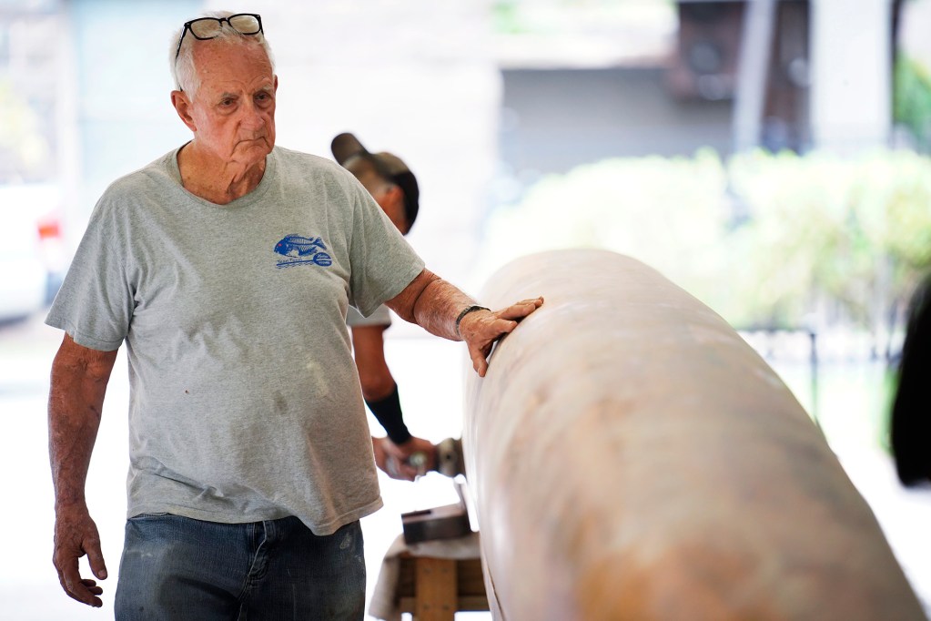 Tay Perry feels for imperfections on Prince Jonah Kūhiō Kalanianaʻole’s a‘a before applying its final coat Monday, Nov. 3, 2025, at the Bishop Museum in Honolulu. The 40-foot racing canoe will return to the water for the first time in more than a decade. (Kevin Fujii/Civil Beat/2025)