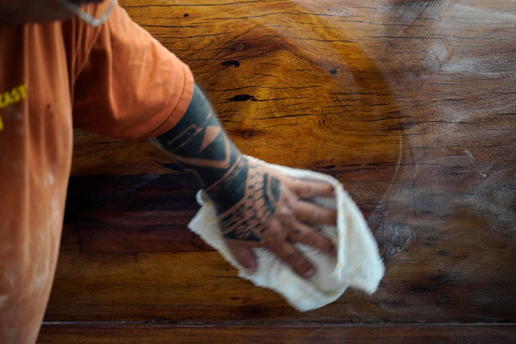Ryan Olivares wipes off dust after sanding Prince Jonah Kūhiō Kalanianaʻole’s a‘a before applying its final coat Monday, Nov. 3, 2025, at the Bishop Museum in Honolulu. The 40-foot racing canoe will return to the water for the first time in more than a decade. (Kevin Fujii/Civil Beat/2025)