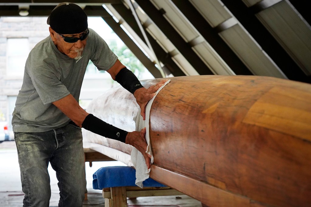 Billy Richards wipes down Prince Jonah Kūhiō Kalanianaʻole’s a‘a before applying its final coat Monday, Nov. 3, 2025, at the Bishop Museum in Honolulu. The 40-foot racing canoe will return to the water for the first time in more than a decade. (Kevin Fujii/Civil Beat/2025)