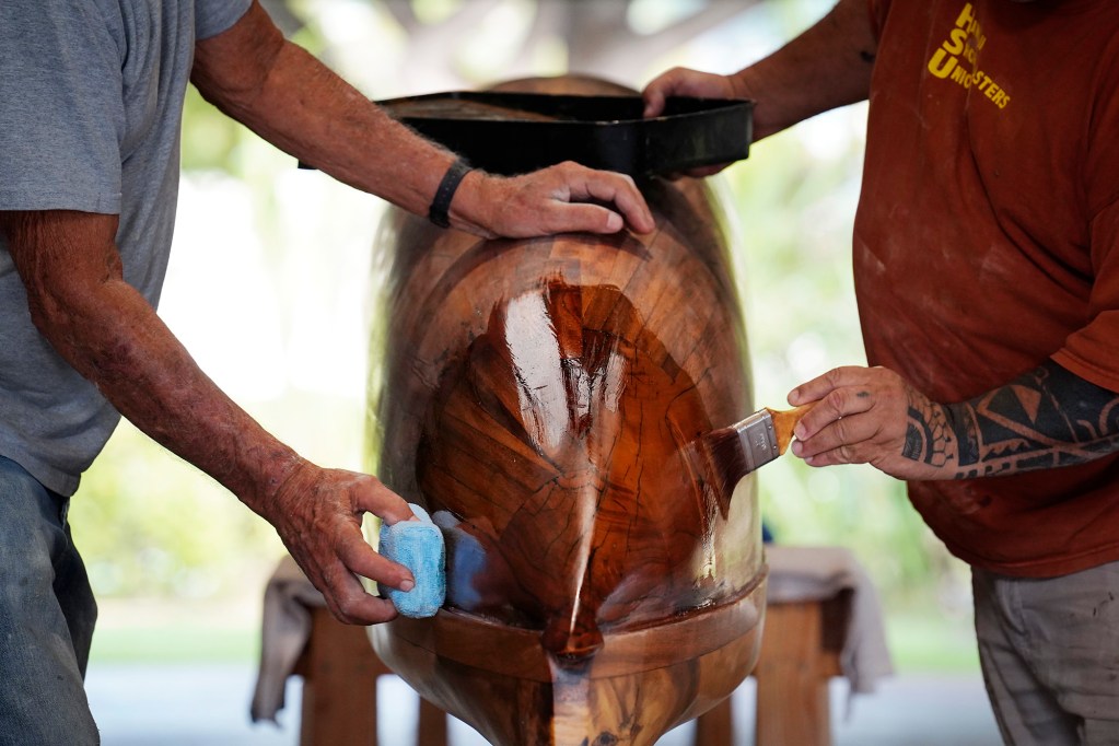 Tay Perry, left, and Ryan Olivares apply the final coat to Prince Jonah Kūhiō Kalanianaʻole’s a‘a Monday, Nov. 3, 2025, at the Bishop Museum in Honolulu. The 40-foot racing canoe will return to the water for the first time in more than a decade. (Kevin Fujii/Civil Beat/2025)