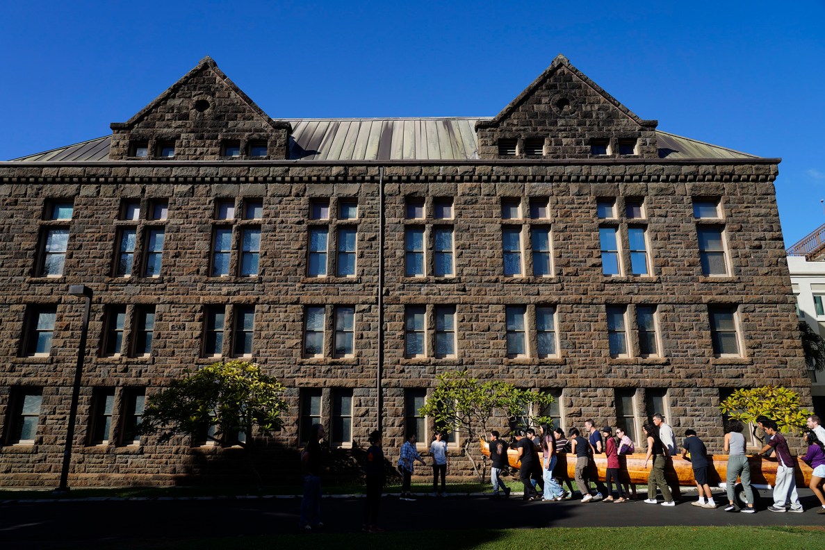 Farrington High School students help move Prince Kūhiō’s A‘a at Bishop Museum to to a trailer Friday, Nov. 7, 2025, in Honolulu. It’s being moved to Ke‘ehi Lagoon for a ceremonial blessing and paddle. (Kevin Fujii/Civil Beat/2025)