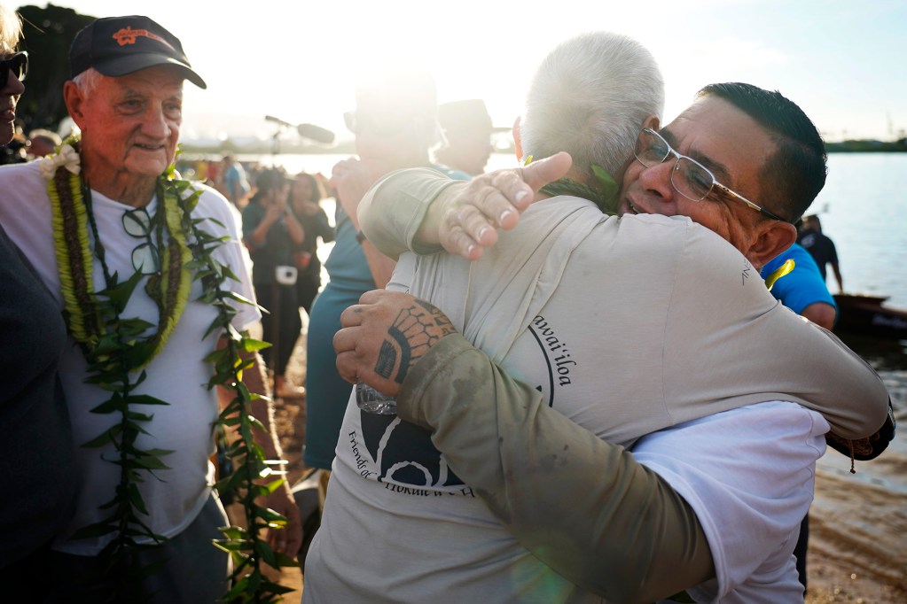 Tay Perry, from left, looks on as Billy Richards hugs Perry’s apprentice Ryan Olivares after the A‘a’s inaugural paddle at Ke‘ehi Lagoon Saturday, Nov. 8, 2025, in Honolulu. (Kevin Fujii/Civil Beat/2025)