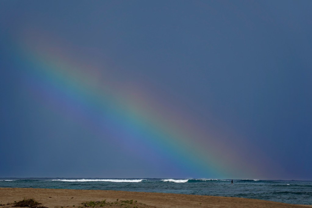 An e-foiler flies at the base of a rainbow over Hanalei Bay Wednesday, Nov. 19, 2025, in Hanalei. This is near the surf break where off-duty Kauaʻi lifeguard Chance Swanson, 33, was bitten by a shark on Nov. 5, 2025. (Kevin Fujii/Civil Beat/2025)