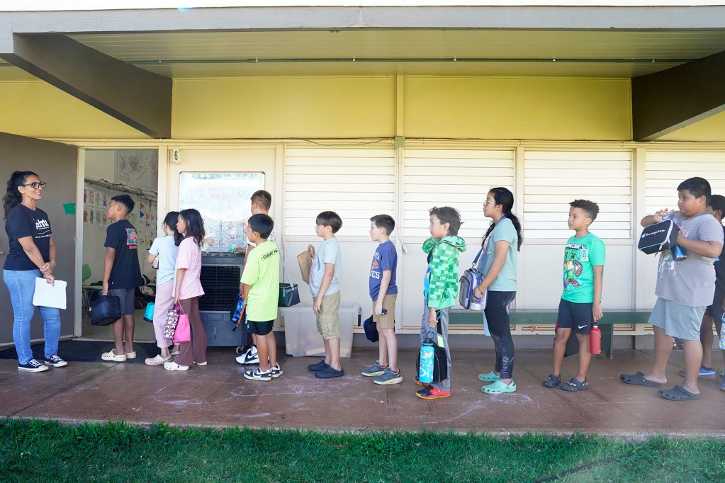 4th graders form a a line in front of their teacher at the entrance to a classroom.