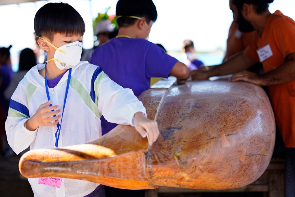 Kapālama Elementary School 4th grader Changqiu Wang sands Keaolewao Kalihi wooden wa‘a during the Ho‘ākea Honolulu hands-on learning and experiencing event centered around traditional Hawaiʻian navigation and voyaging canoes Wednesday, Dec. 3, 2025, in Honolulu. Hawaiʻian voyaging traditions, cultural practices and ʻāina-based learning pairs with DOE curriculum to create a “Navigator Mindset”. (Kevin Fujii/Civil Beat/2025)