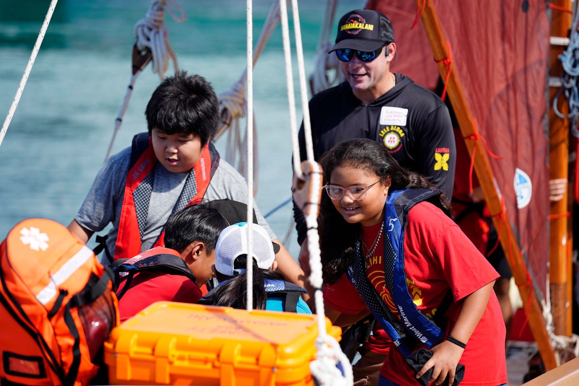 Lele Aloha’s Ka‘anapu Kalama-Jacobsen, in black, guides Kalihi Kai Elementary School 4th graders to move the hoe uli (rudder paddle) on the Mānaiakalani voyaging canoe during the Ho‘ākea Honolulu hands-on learning and experiencing event centered around traditional Hawaiʻian navigation and voyaging canoes Wednesday, Dec. 3, 2025, in Honolulu. Hawaiʻian voyaging traditions, cultural practices and ʻāina-based learning pairs with DOE curriculum to create a “Navigator Mindset”. (Kevin Fujii/Civil Beat/2025)