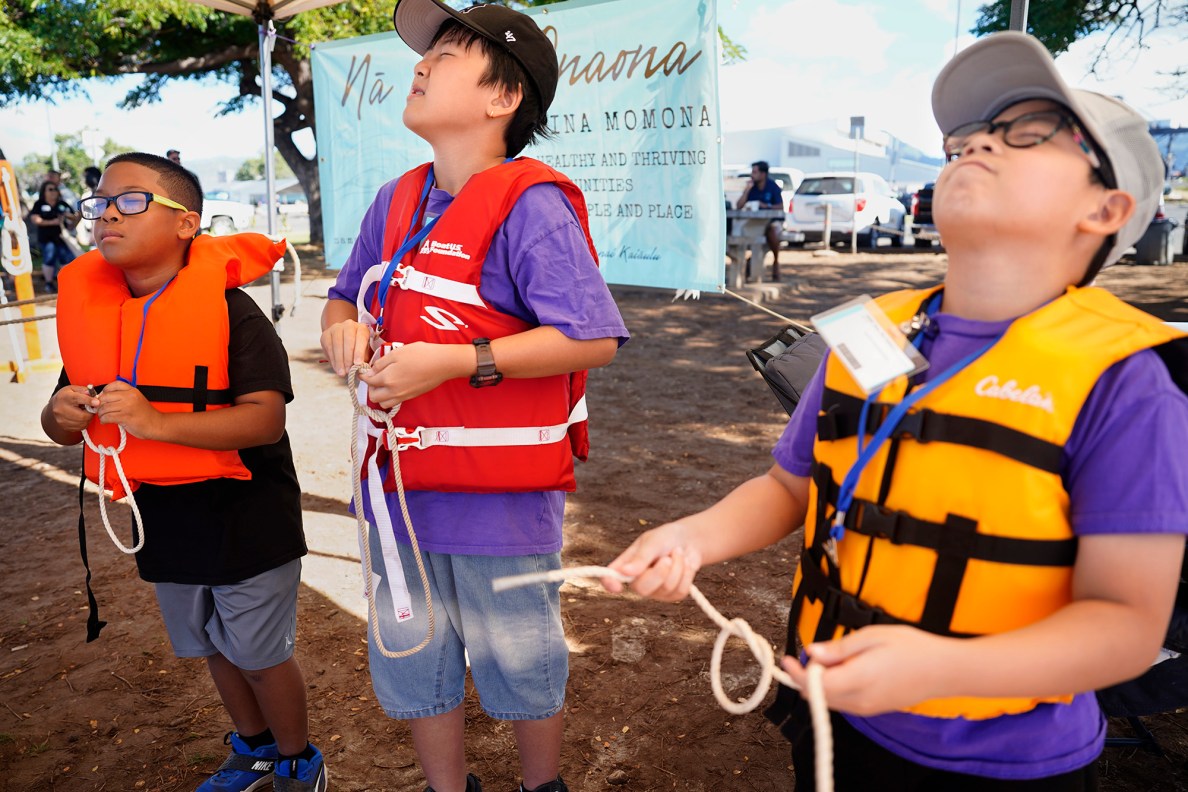 Kapālama Elementary School 4th graders Rixon Allgood-Pascual, from left, Johnny Chen and Kian Reyes close their eyes to mimic nighttime while trying square knots during the Ho‘ākea Honolulu hands-on learning and experiencing event centered around traditional Hawaiʻian navigation and voyaging canoes Wednesday, Dec. 3, 2025, in Honolulu. Hawaiʻian voyaging traditions, cultural practices and ʻāina-based learning pairs with DOE curriculum to create a “Navigator Mindset”. (Kevin Fujii/Civil Beat/2025)
