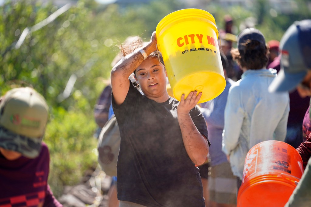 Moʻokuapā volunteer Isabelle Colorado carries a bucket of ko‘a (coral) pieces Saturday, Dec. 13, 2025, in Kāneʻohe. Colorado, who is stationed on Oʻahu with the military and came on her own, is one of 2,000 volunteers who joined the Moʻokuapā community work day to finish the wall of the 800-year-old He‘eia loko i‘a (fishpond). (Kevin Fujii/Civil Beat/2025)