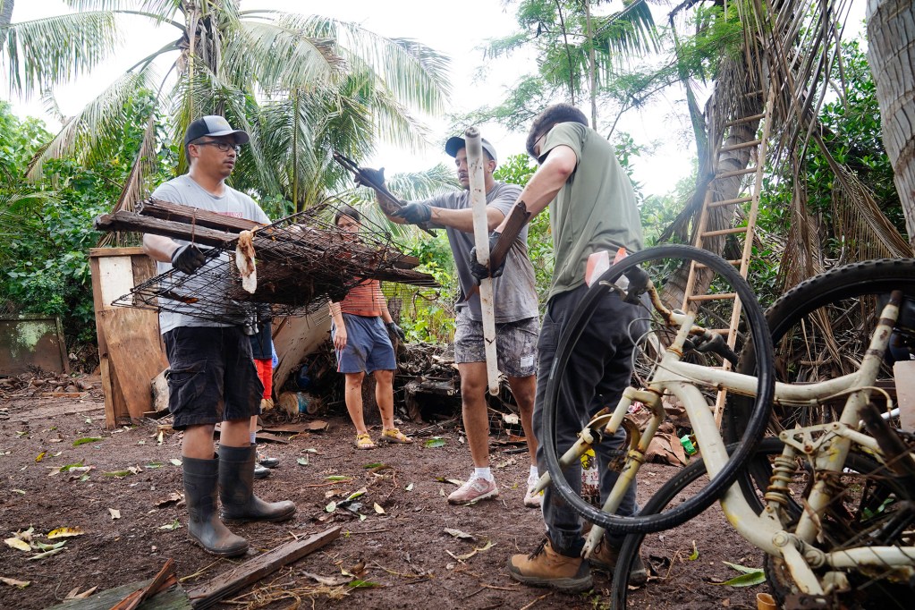 Les Romero, left, gets loaded up with debris by volunteers helping him clear his and his mother Loreta Romero’s  Kukea Loop home Sunday, March 22, 2026, in Waialua. A second Kona low storm brought heavy rain after the previous week’s downpour and high winds. Her son Les Romero’s phone number is 808-772-0313. (Kevin Fujii/Civil Beat/2026)