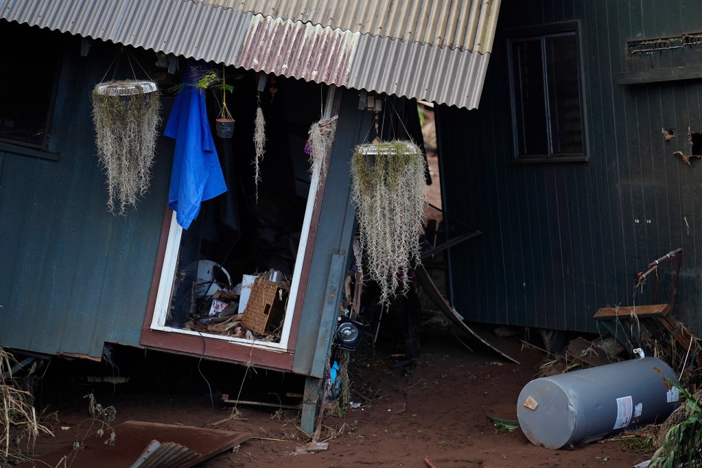 Hanging plants show the correct vertical orientation compared to askew Otake Camp homes which were dislodged from their foundations during a Kona Low storm flood Wednesday, March 25, 2026, in Waialua. The former plantation residential neighborhood received damage from the second Kona Low storm. (Kevin Fujii/Civil Beat/2026)