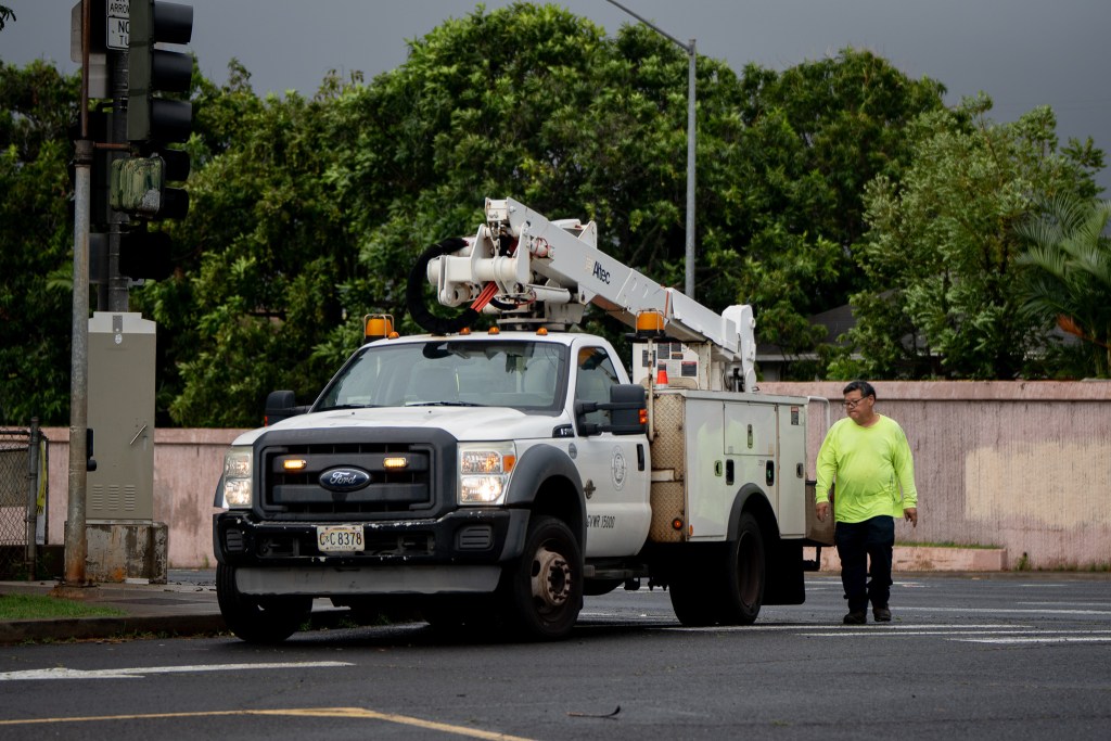 A City & County worker walks next to white bucket truck. The man wears a neon yellow shirt.