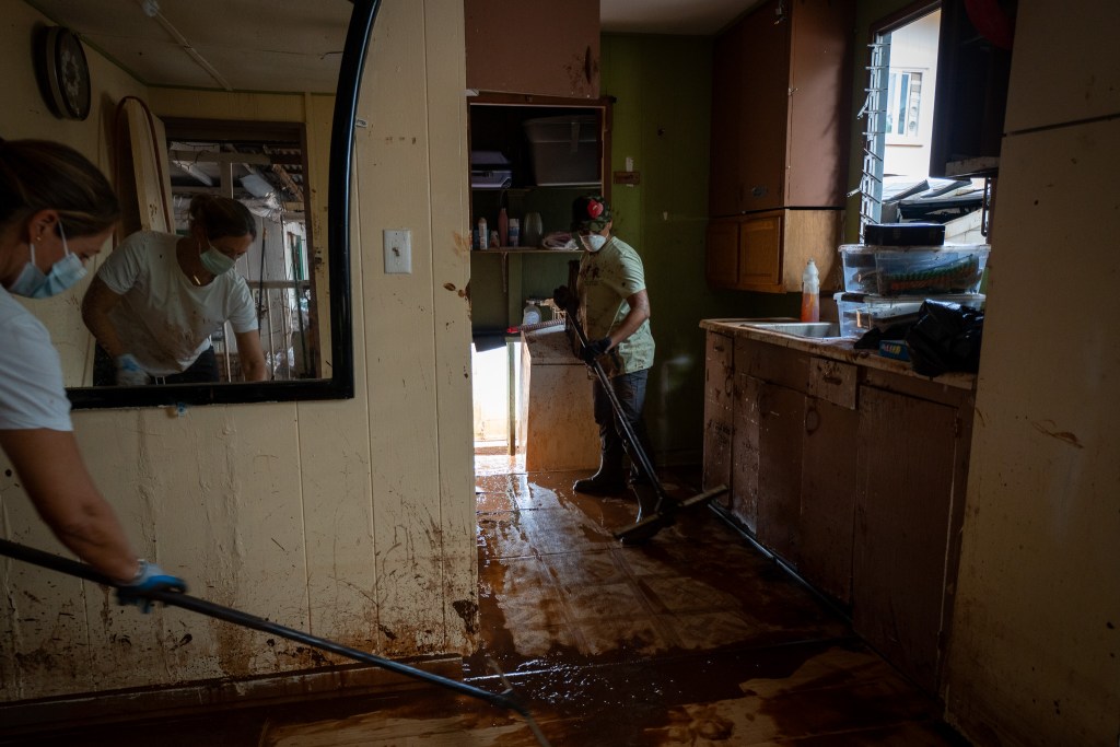 Nicole Fernandez, left, is reflected in a mirror as she and Vanessa Vizcarra volunterred to clean up Estrelita Andres' house on Waialua Beach Road March 24, 2026. Like the majority of volunteers, the two did not know the home owner. Heavy rainfall the last two weeks caused devastating flooding to area residents. (Craig Fujii/Civil Beat/2026)