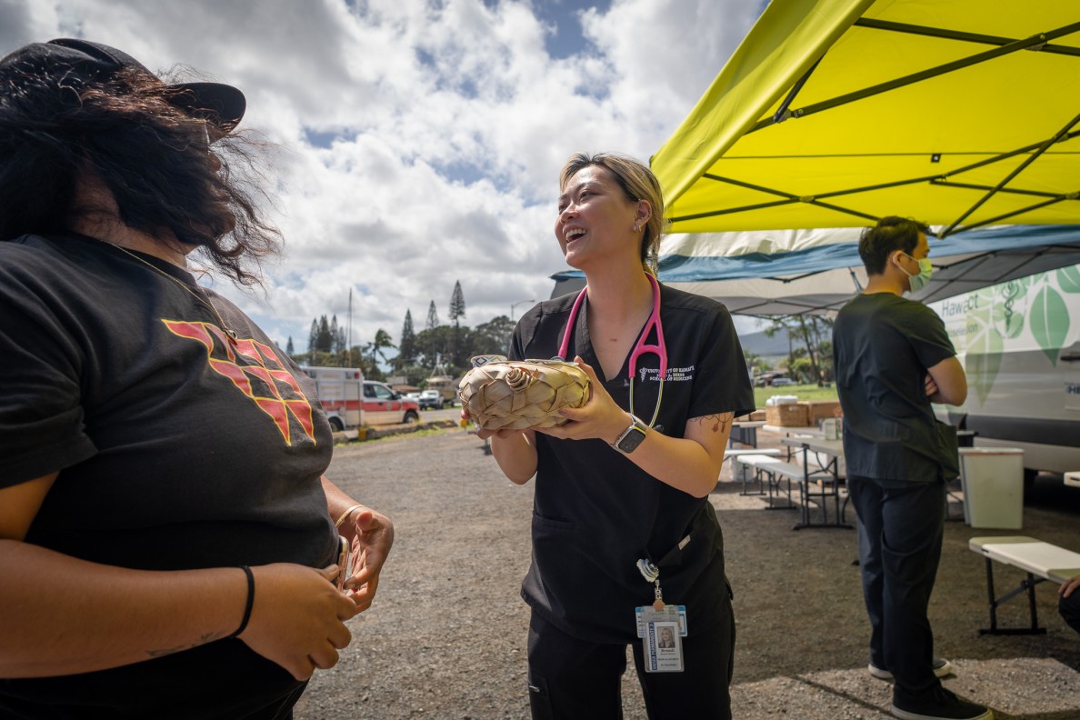 Student doctor Tracie Okumura, receives a woven bowl of coffee cups from Andreanna Kaluhiokalani, left, as she and other students from John A. Burns School of Medicine provided on-site care to local residents at Ali'i Beach Park in flood-ravaged Haleiwa March 26, 2026. Kaluhiokalani's family owns the coffee shop, Love Like Buttons. (Craig Fujii/Civil Beat/2026)