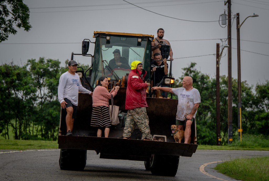 Evacuated residents catch a ride on a bulldozer at Haleiwa March 20, 2026. Saturated ground and more rain overnight caused flooding in Haleiwa and Waialua. (Craig Fujii/Civil Beat/2026)