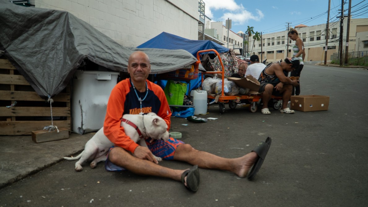 Mike Padua, 47, sits with his six-month-old dog, Jovaiah, across the street from Punawai Rest Stop in Iwilei. The rest stop provides hygiene services, laundry and social services.