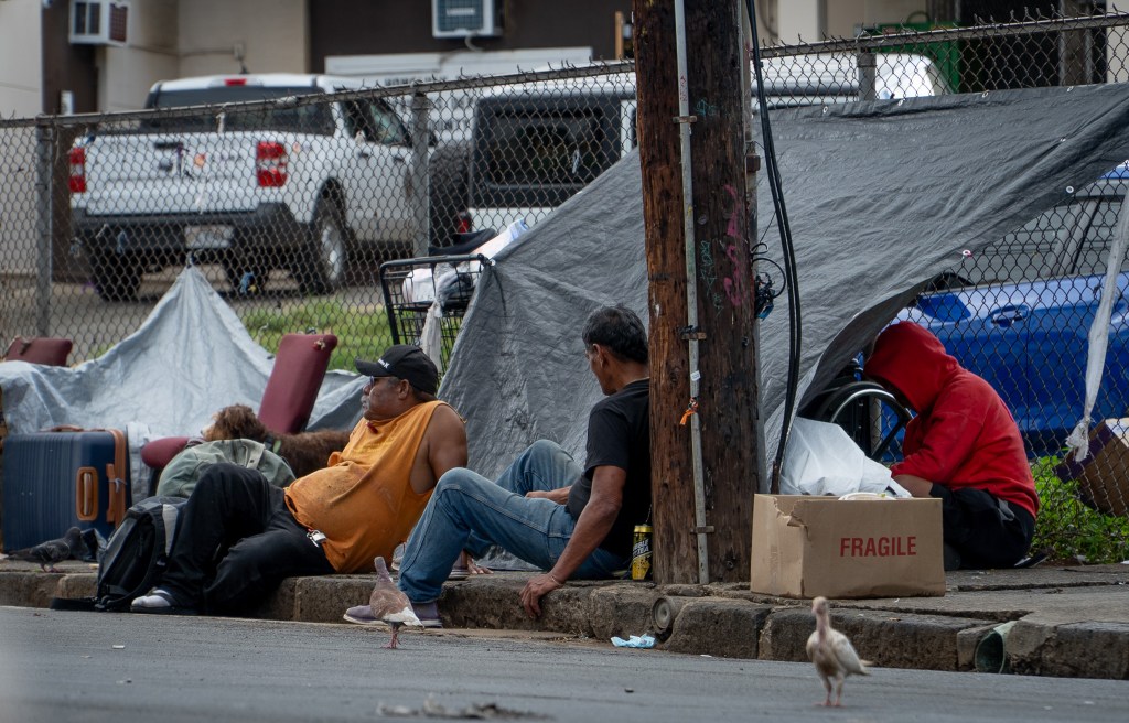 14:43 Men sitting on a sidewalk next to Punawai Rest Stop in Iwilei, Monday. The rest stop provides hygiene facilities, cellphone charging, laundry and social services.