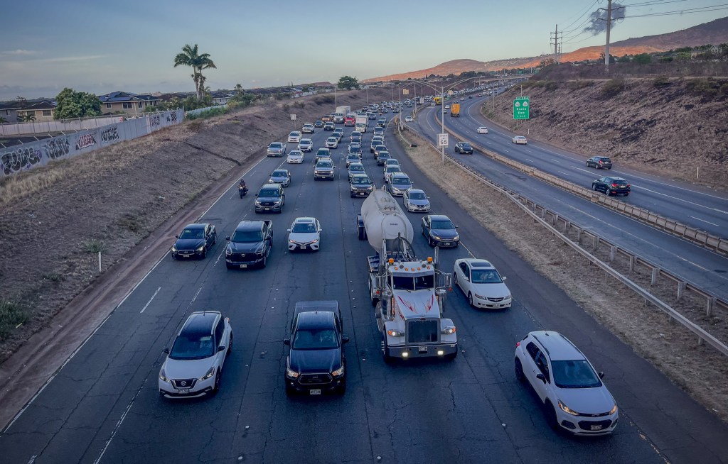 An overhead view of a highway showing five lanes of vehicles facing the camera. The road recedes into the background, curving to the right.