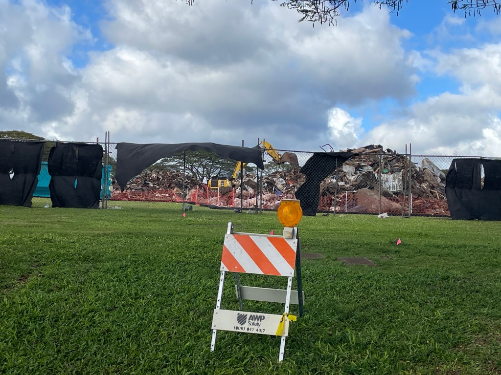 Black screens hanging on a barrier fence that surrounds tons of flood debris from the March 20206 storms on Oahu.