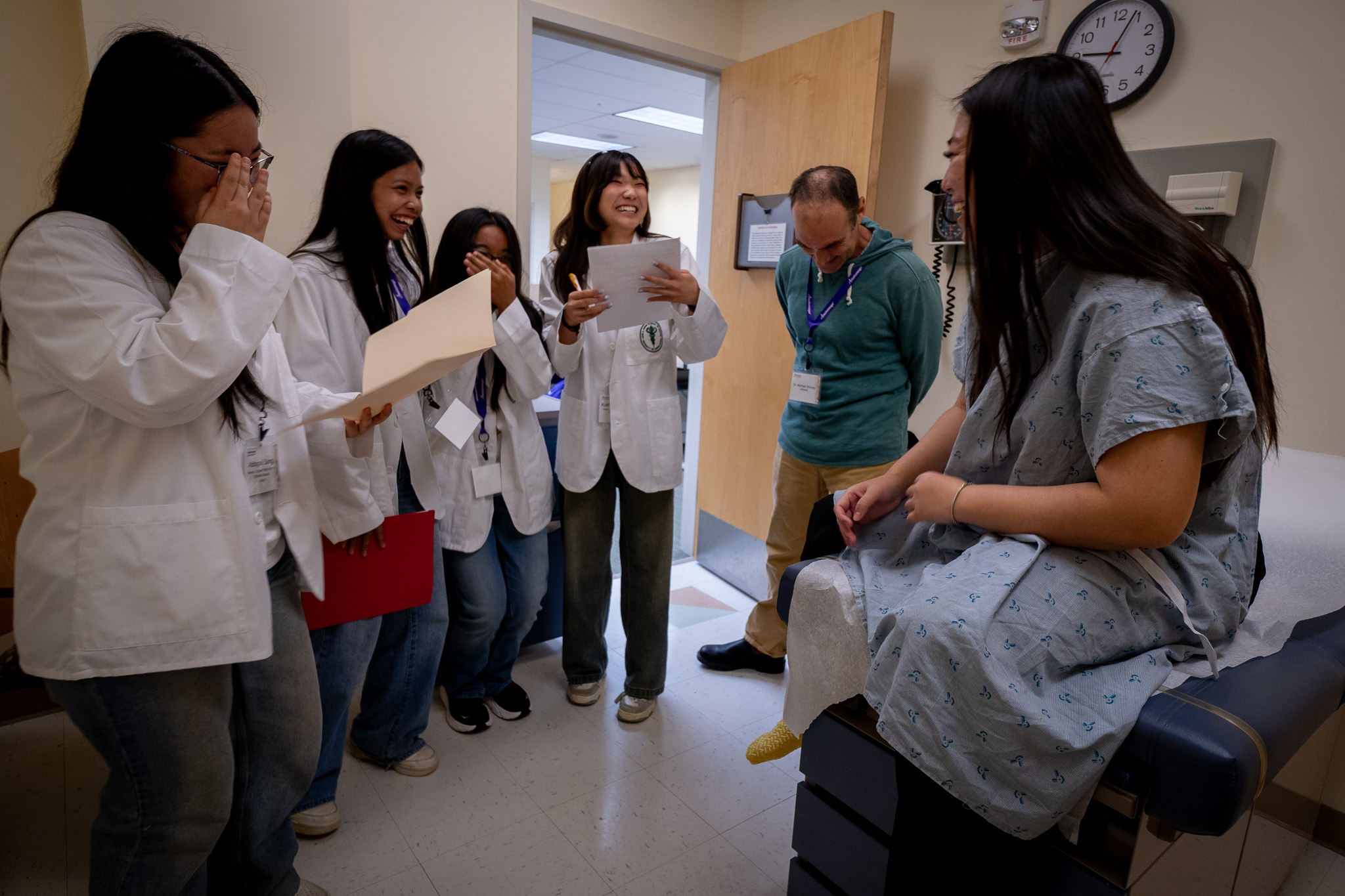Student doctor Darcy Tokunaga, right, shares a laugh with Kaiser High School students as she plays a sick patient during an educational event at JABSOM April 7, 2026. From left are Abbigail Song, Kailie Arpin, Mia Meeds, Kaitlin Miyashiro and Dr. Michael Wyman. The event and competition featured virtual cadaver tables created by Anatomage of Santa Clara, Calif. (Craig Fujii/Civil Beat/2026)