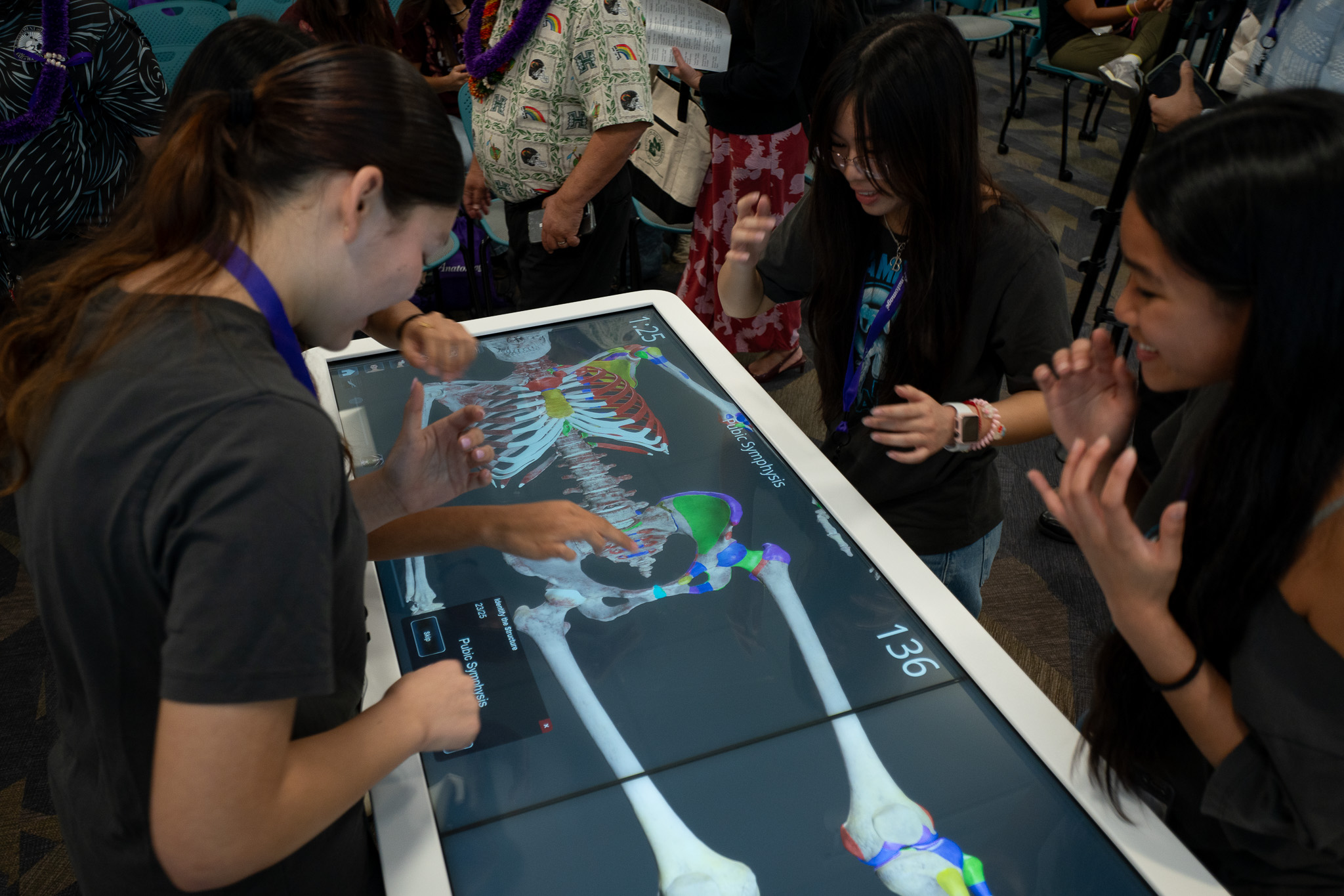Kapolei High School students working with an Anatomage virtual cadaver table at JABSOM April 7, 2026. From left are Anna Steed, Benyapa Martin and Emani Villegas. Faith Antonio is the fourth member of the team and not pictured. (Craig Fujii/Civil Beat/2026)