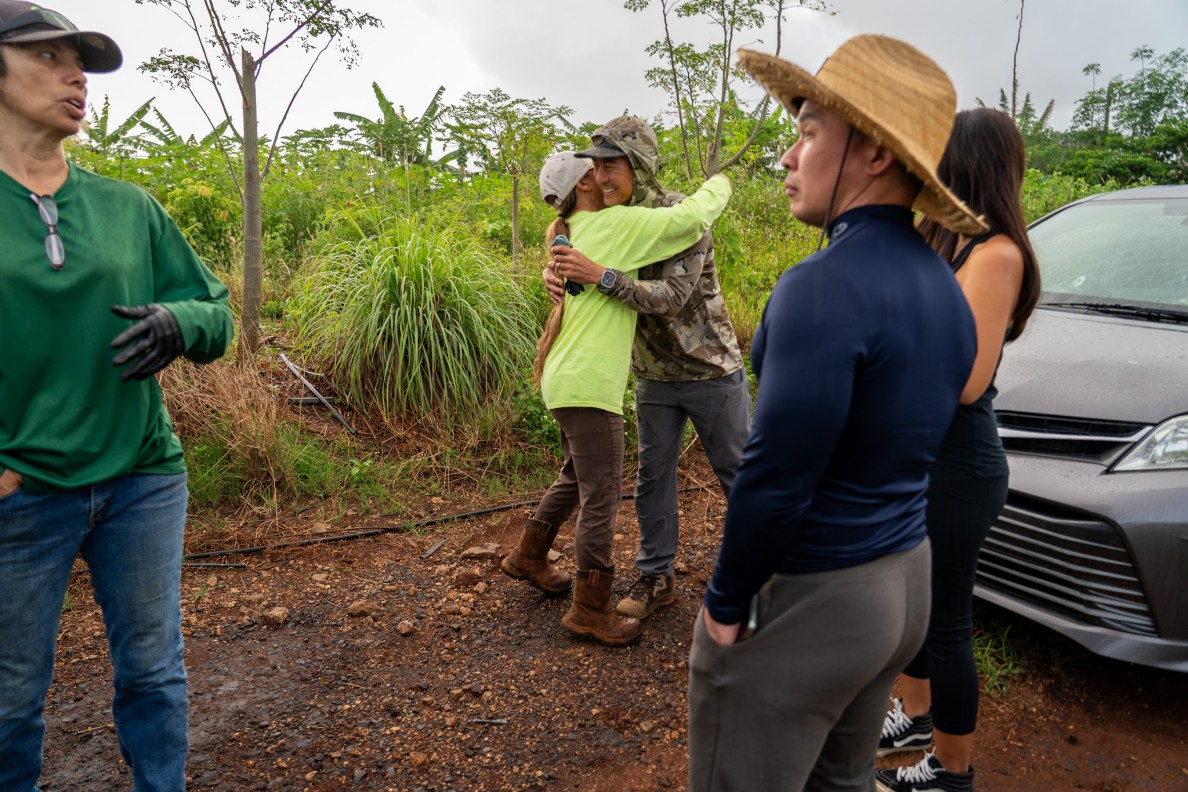 Grace Kekahuna hugs David Taniyama after the two Maryknoll school mates recognized each other decades later at Mill 6 Farms in Waialua May 23, 2026. Kekahuna and the Waialua Farmers Cooperative arranged a work day to clear ditches to improve water flow after the Kona low storms, which flooded the area. Michelle Midro Ching, left, and Drew Enomoto, right. (Craig Fujii/Civil Beat/2026)
