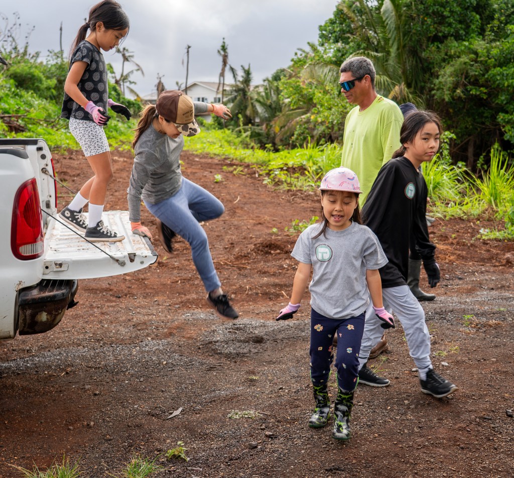 Julie Taniyama leaps off a pickup at Mill 6 Farms in Waialua May 23, 2026 followed by her daughter Sarah. Taniyama and church members from Wellspring Covenant Church volunteered to help clean ditches at the farm. (Craig Fujii/Civil Beat/2026)