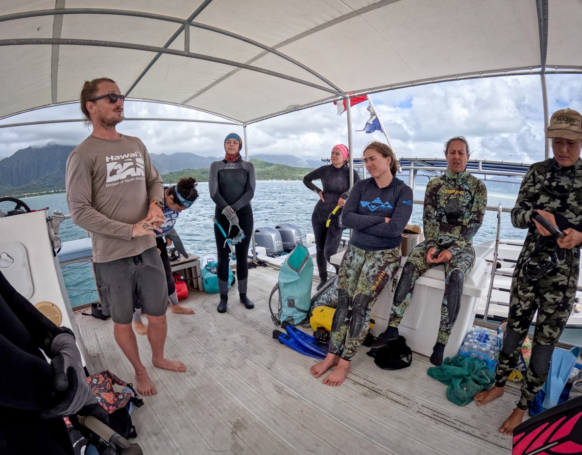 DAR's Jesse Boord, left, debriefs stakeholders during a visit to Reef Eight at Kāneʻohe Bay May 28, 2026. An invasive species of anemone was discovered at the site and DAR and other agencies are working to eradicate the pest, which will damage coral colonies. (Craig Fujii/Civil Beat/2026)