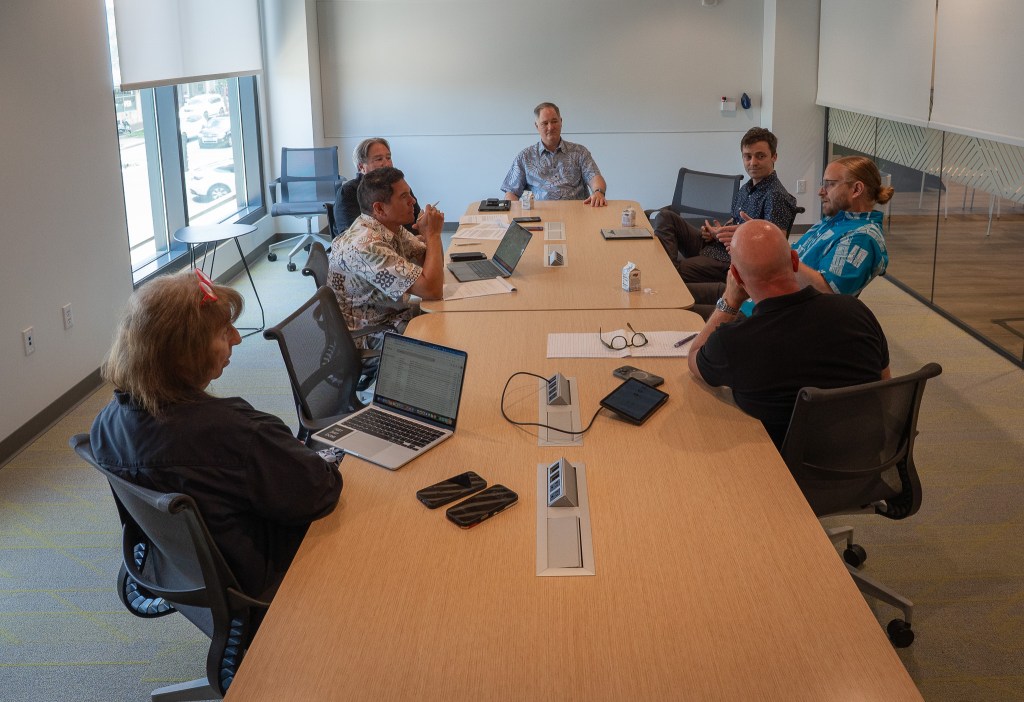 Individuals sitting in a conference room at a light wood table.