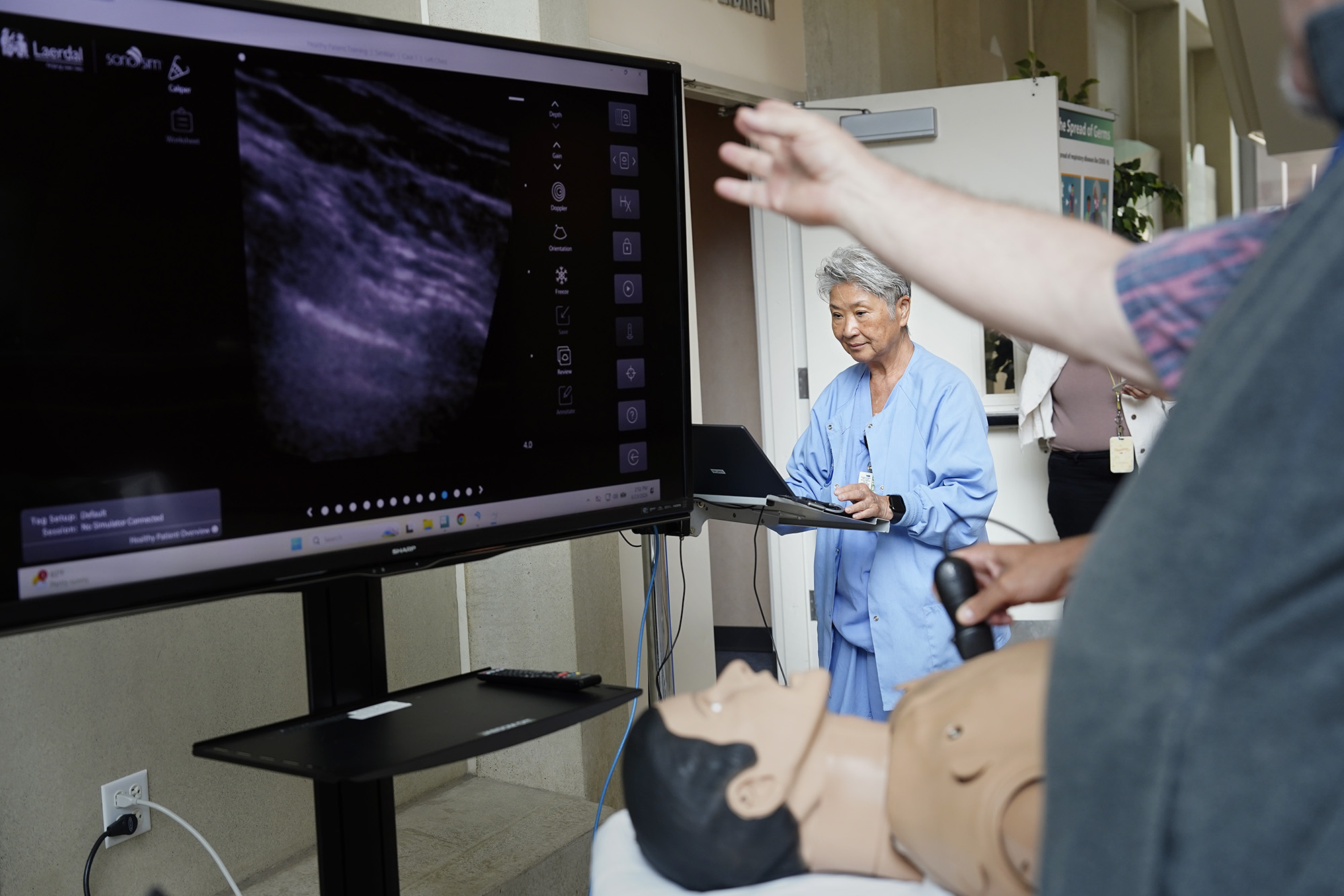 The University of Hawaiʻi John A. Burns School of Medicine’s SimTiki Simulation Center’s operations director Kris Hara checks the vitals of their newly acquired ultrasound “manikin” or human patient simulator, Tuesday, June 23, 2026, in Honolulu. This manikin, spelled differently from mannequin which is used for modeling clothes, shows real, internal, human images programmed into the device as a medical student manipulates the ultrasound transducer. (Kevin Fujii/Civil Beat/2026)