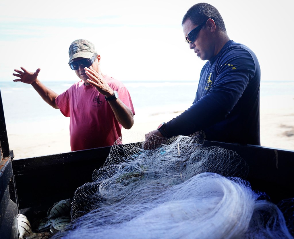 Keli‘i Alapa‘i, left, makes the internationally known sign for the size of the fish he almost caught while his son Kanoe Alapai-Hashimoto untangles some of the manini they caught in Hāʻena community fishing waters Sunday, June 28, 2026, in Hāʻena.