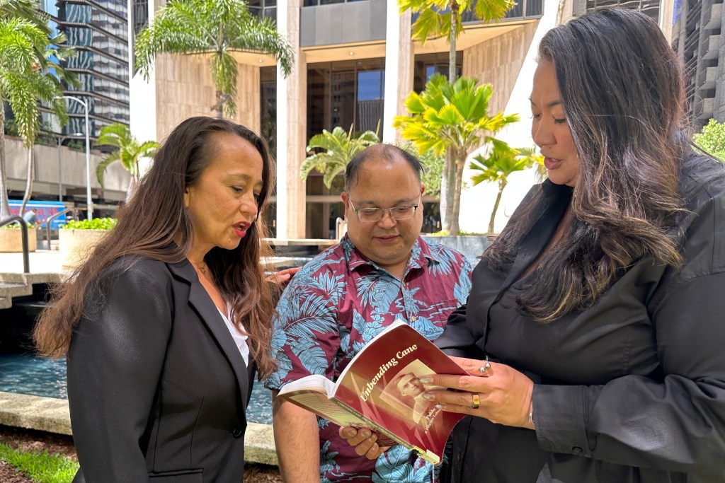 Attorneys Becky Gardner, left, Daniel Padilla, center, and Kainani Collins Alvarez look through a book about Filipino labor leader Pablo Manlapit on Wednesday, May 27, 2026, in Honolulu. (AP Photo/Jennifer Sinco Kelleher)
