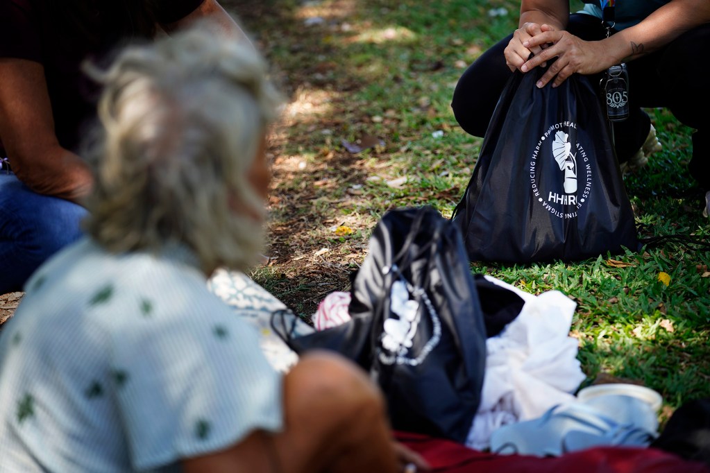 Bags filled with necessities are handed out by Hawaiʻi Health and Harm Reduction Center’s Housing and Outreach Manager Michelle Wilkins and Youth Services Navigator Ashley Rueda to homeless Tuesday, July 21, 2026, at Ala Moana Regional Park in Honolulu. Their program, Guide on the Side, is an outreach program which focuses on at-risk,  homeless youth, especially LGTBQ+ kids. Local homeless service providers are uncertain about if their federal funding will be renewed after the federal government changed funding policies, guidelines and priorities. (Kevin Fujii/Civil Beat/2026)
