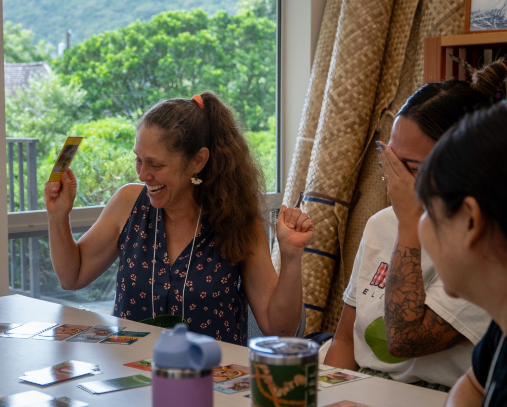 Teachers Kim Richmond, left, and Danielle Montano (covering her face) find success playing Kumala'au, a card game teaching about flora, culture and environmental stewardship at Mānoa Heritage Center July 9, 2026. About 20 local teachers participated. (Craig Fujii/Civil Beat/2026)