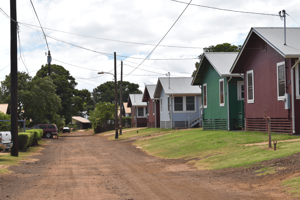 A row of red, light blue and green recently rebuilt homes along a dirt road in Kaumakani Camp on Kaua‘i's West Side.
