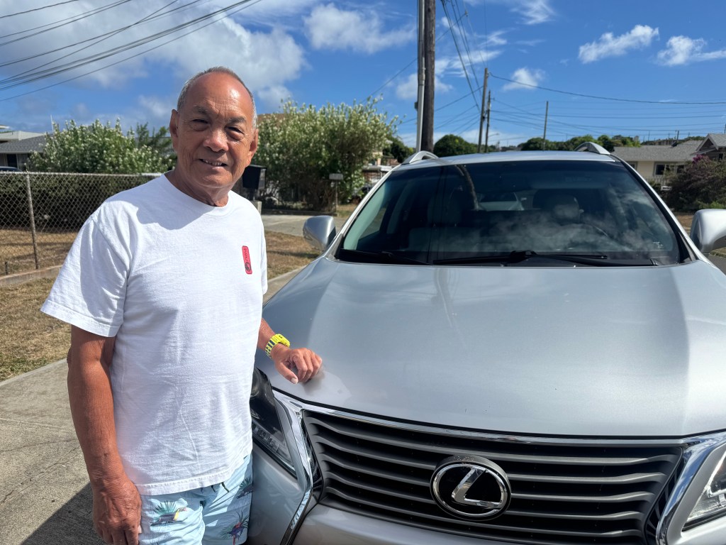 A man stands in front of his SUV at the curb outside his house.