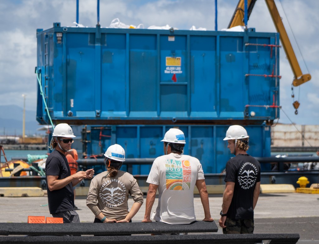 Kevin O'Brien, left, and crewmembers pause while a container of marine debris is unloaded at Pier 34 August 28, 2026. The Papahānaumokuākea Marine Debris Project, a non-profit, collected 48,000 pounds of debris on a mission interrupted by Hurricane Lala. (Craig Fujii/Civil Beat/2026)