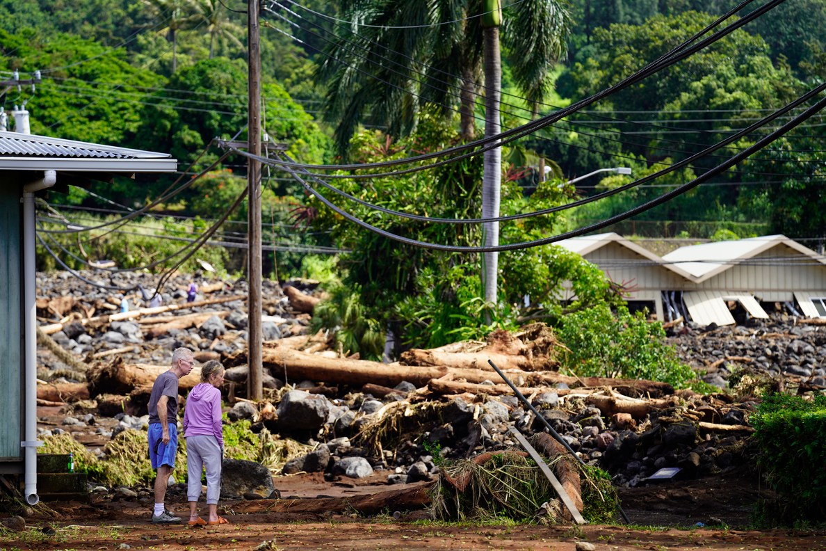 People look at Kaʻalaiki Road leading to the Nāʻālehu Cemetery and mauka which lie washed out and covered in rubble Tuesday, Aug. 18, 2026, on Hawaiʻi Island. The building behind them is the Nāʻālehu Ace Hardware. Hurricane Lala made a close pass to the South Point of the Big Island Saturday. (Kevin Fujii/Civil Beat/2026)