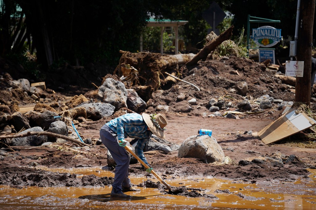 A resident who wished to be identified as Na Wahine Koi shovels mud from the intersection of Hawaiʻi Belt Road and Kaʻalaiki Road in the town of Nāʻālehu Tuesday, Aug. 18, 2026, on Hawaiʻi Island. Hurricane Lala made a close pass to the South Point of the Big Island Saturday. (Kevin Fujii/Civil Beat/2026)