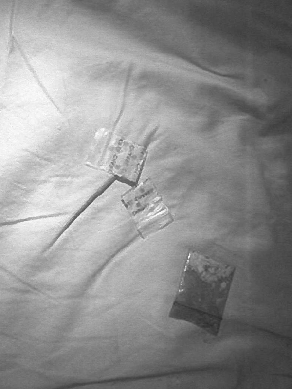 Three little resealable baggies with white substance on top of white bed sheets.
