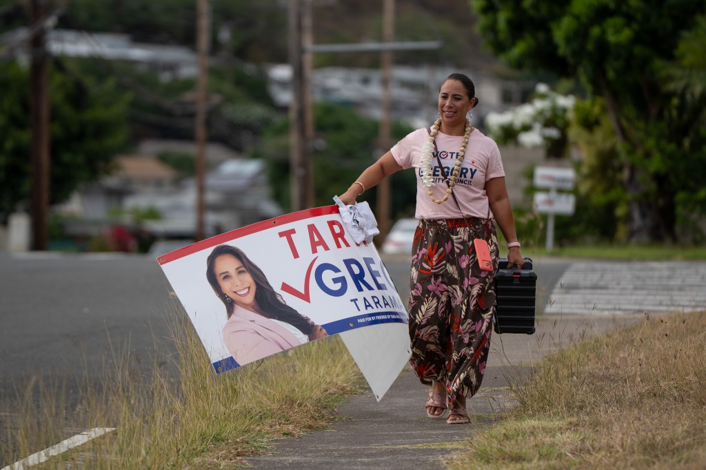 District IV council candidate Tara Malia Gregory carries a campaign sign to a sign waving site in Hawaiʻi Kai August 5, 2026. (Craig Fujii/Civil Beat/2026)