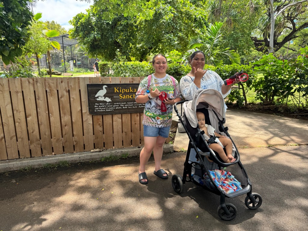 Two young women smile and pose outside at the zoo as they stand behind a stroller
